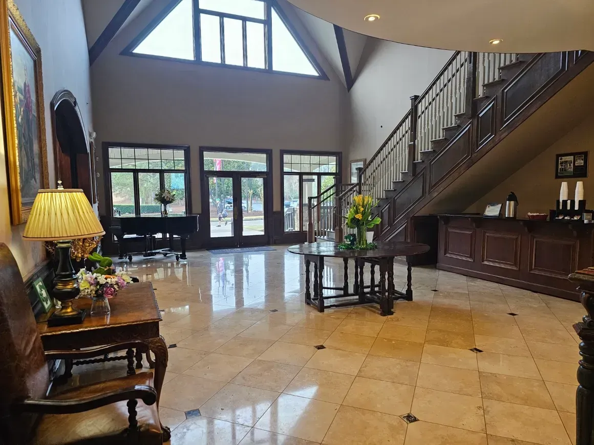 Grand foyer with marble floor, staircase, and a table with flowers.