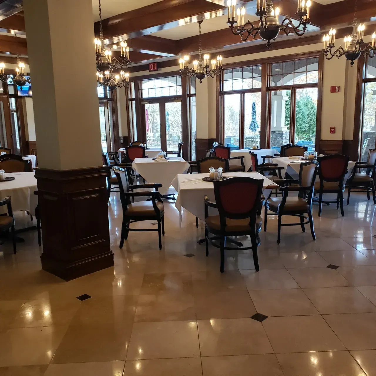 Dining room with tables set for service, chandeliers, large windows, and a marble floor.
