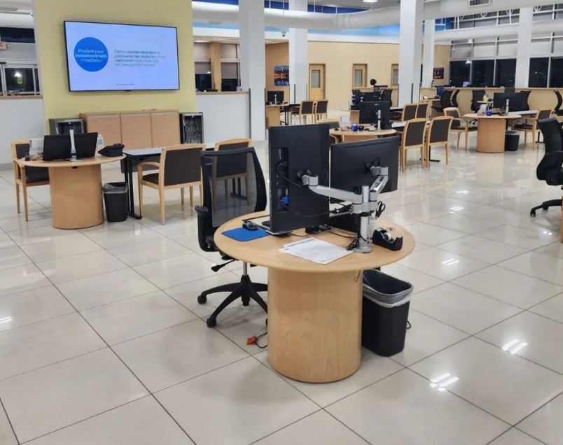 A library interior with computers on round tables, chairs, and a large screen displaying text on the wall. A library interior with computers on round tables, chairs, and a large screen displaying text on the wall.