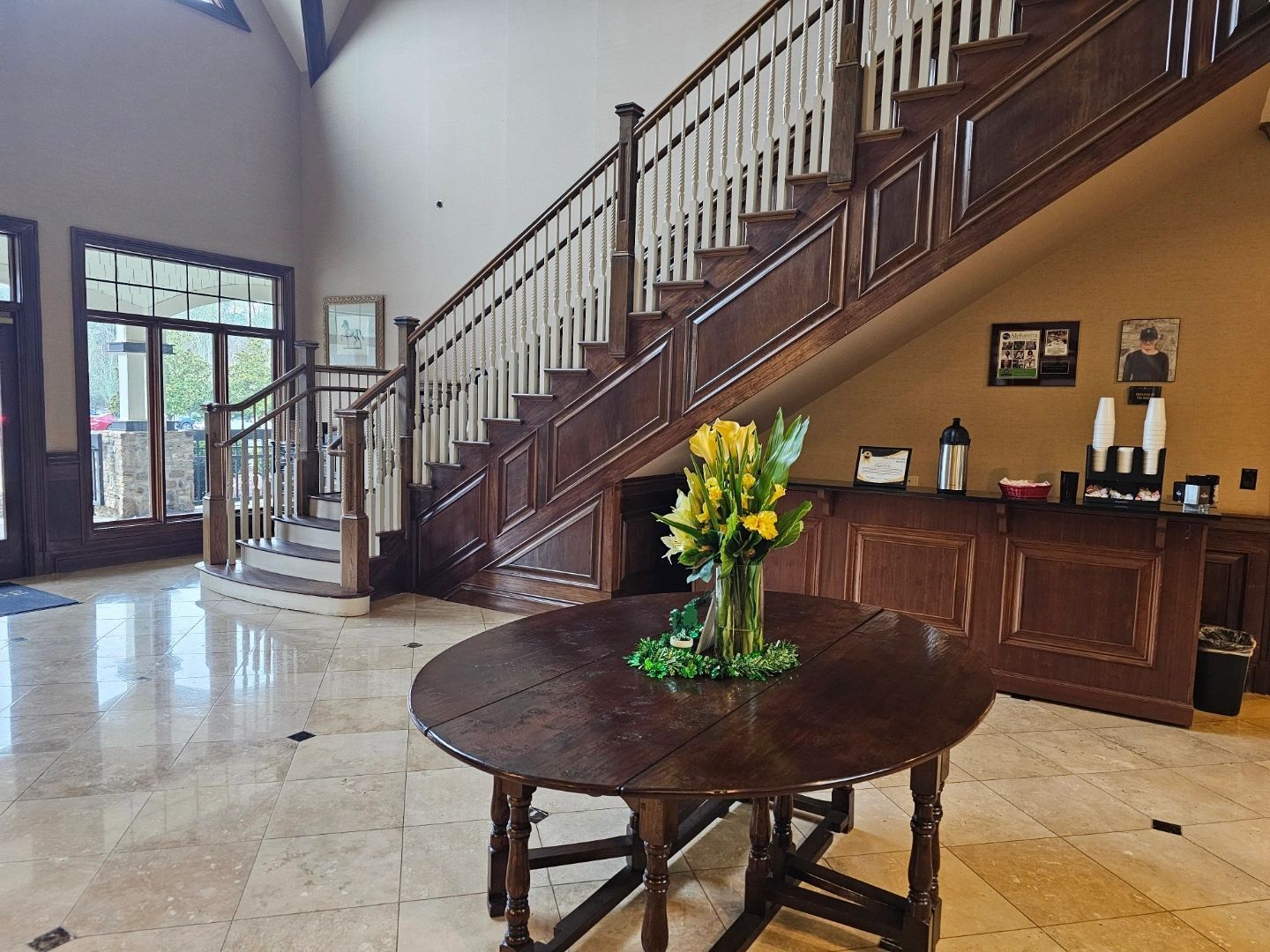 Elegant foyer with grand staircase, wooden accents, and a round table with flowers. Elegant foyer with grand staircase, wooden accents, and a round table with flowers.