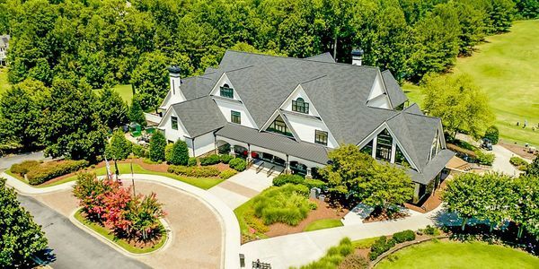 Aerial view of a white building with a dark gray roof surrounded by trees and a golf course. Aerial view of a white building with a dark gray roof surrounded by trees and a golf course.