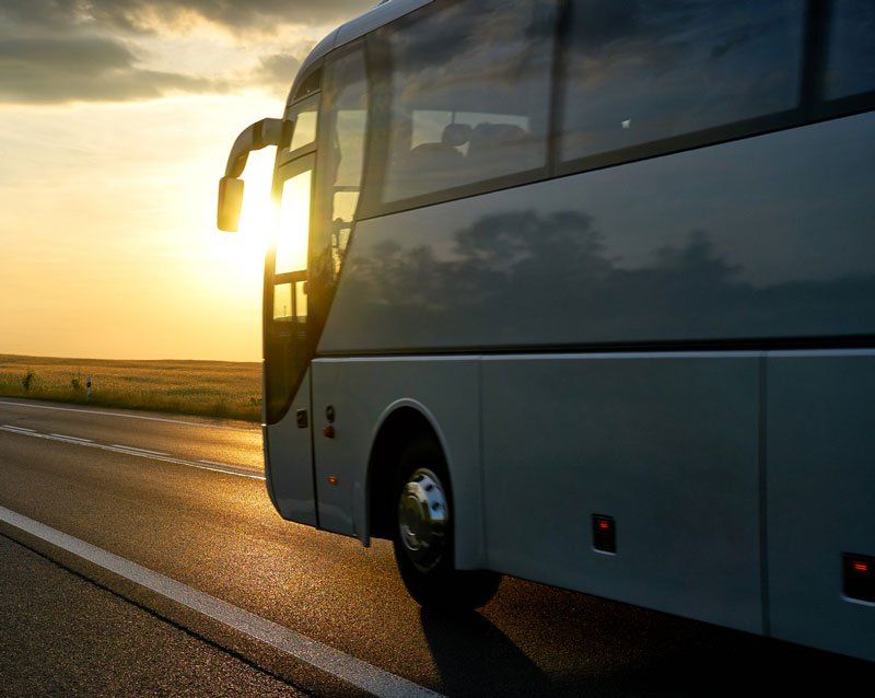 White Bus driving along the asphalt road in a rural landscape at sunset.