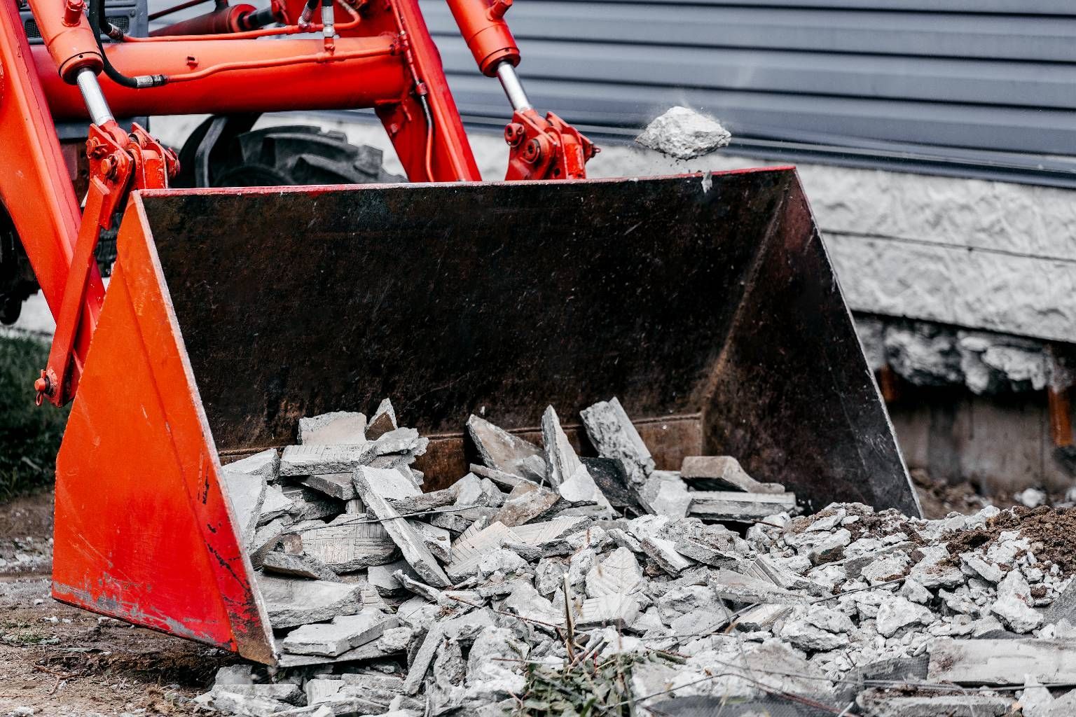 Red construction loader bucket scooping rubble and broken concrete on a work site