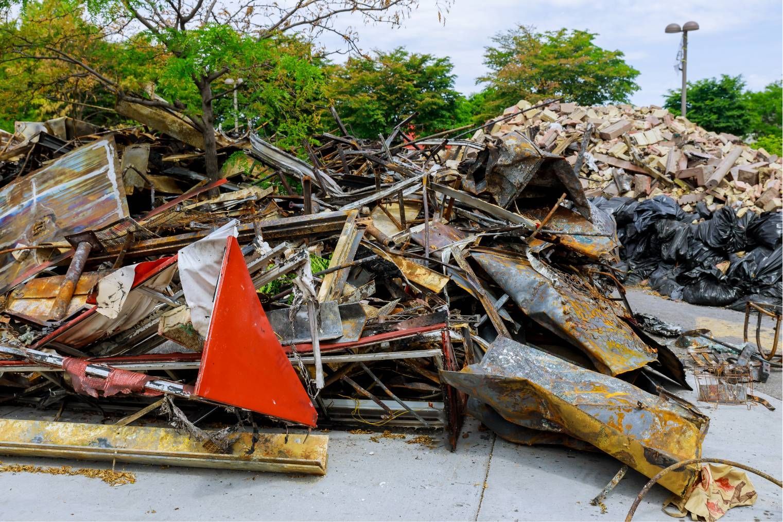 Collapsed debris pile with twisted metal and a bright orange warning cone beside a road