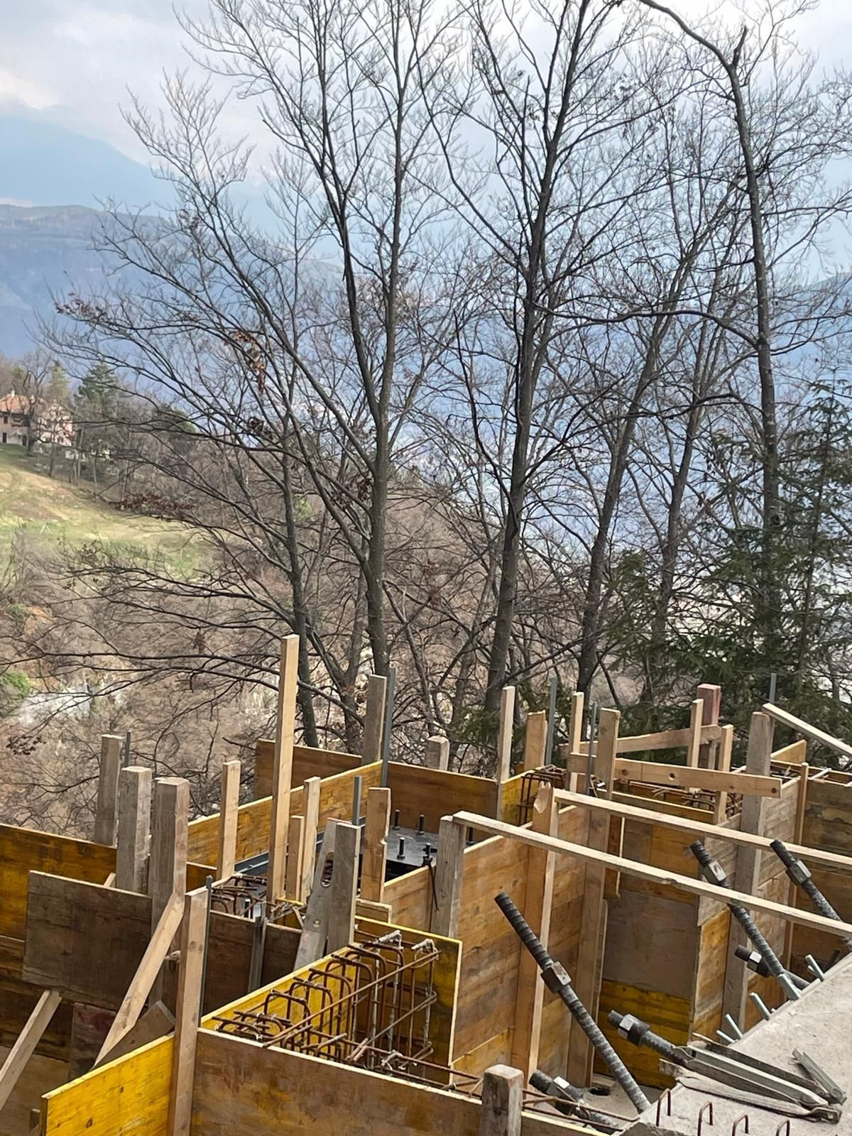 Pannelli di casseratura in legno e gabbia di barre d'acciaio per una fondazione in cemento armato addossata a un pendio collinare con alberi spogli.