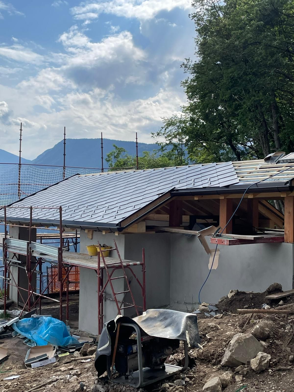 Un piccolo edificio in costruzione con il tetto appena posato, impalcature e montagne sullo sfondo.