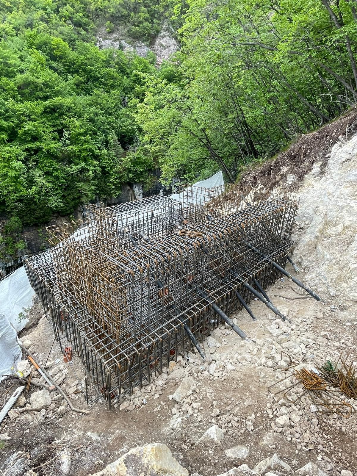 Una gabbia di barre d'acciaio incastonata in un pendio roccioso, a mo' di fondazione per una futura costruzione.