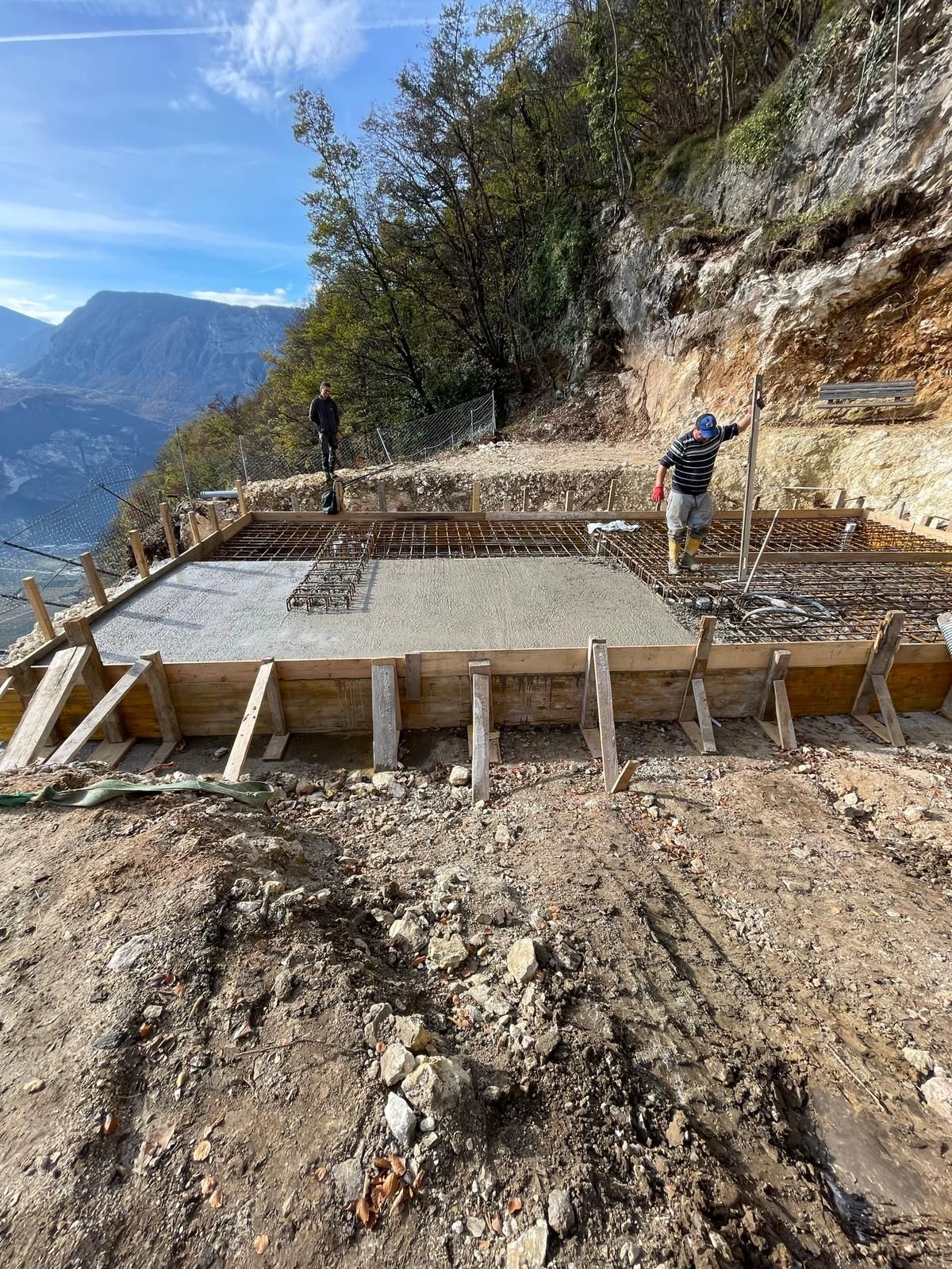 Un cantiere edile su un fianco di montagna, con una struttura di casseratura in legno per una fondazione in cemento armato.
