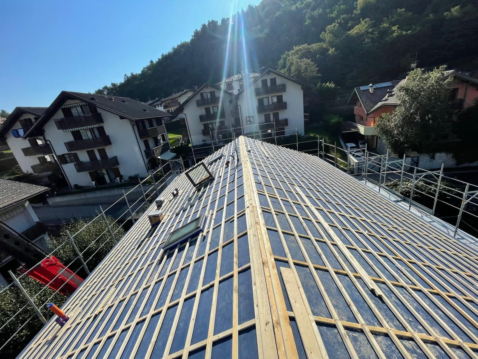 Vista da un tetto in costruzione con listelli di legno installati su una membrana nera, con case sullo sfondo.