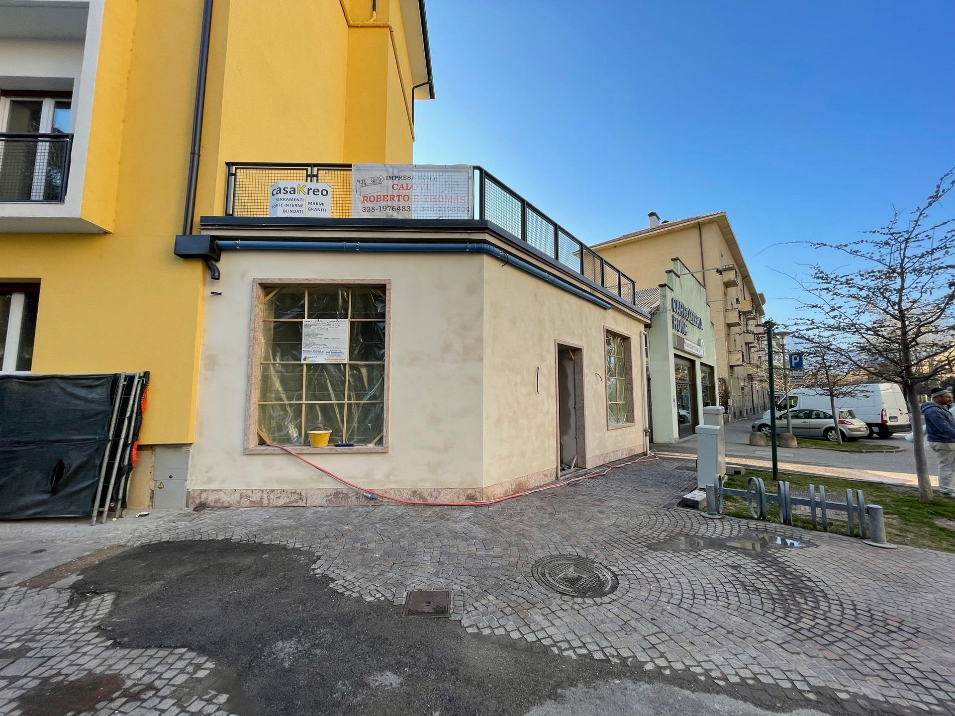 Un piccolo edificio color crema a un solo piano, situato all'angolo di una strada asfaltata, adiacente a un edificio giallo più alto.