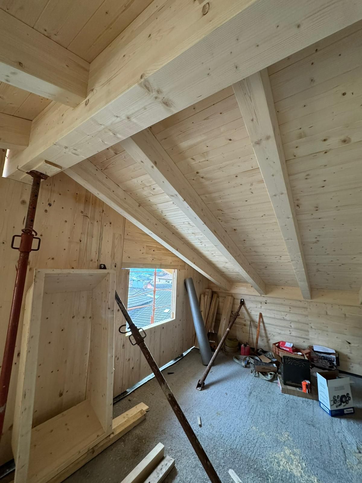 Una soffitta in ristrutturazione con travi di legno a vista, soffitto inclinato, pali di sostegno temporanei e materiali sparsi ovunque.
