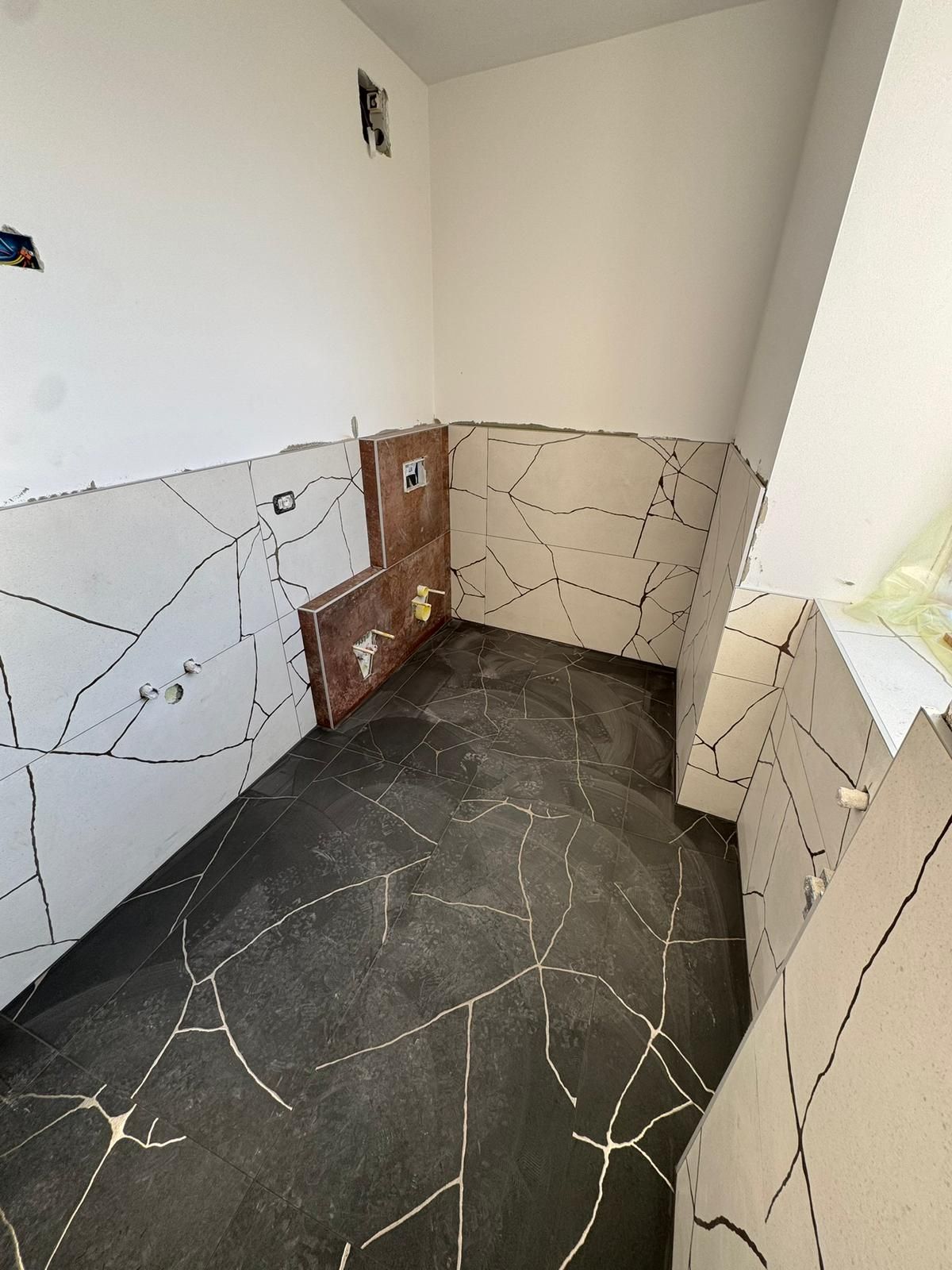 Interno di un bagno non rifinito, caratterizzato da pareti bianche e piastrelle del pavimento con una particolare venatura effetto marmo nera.