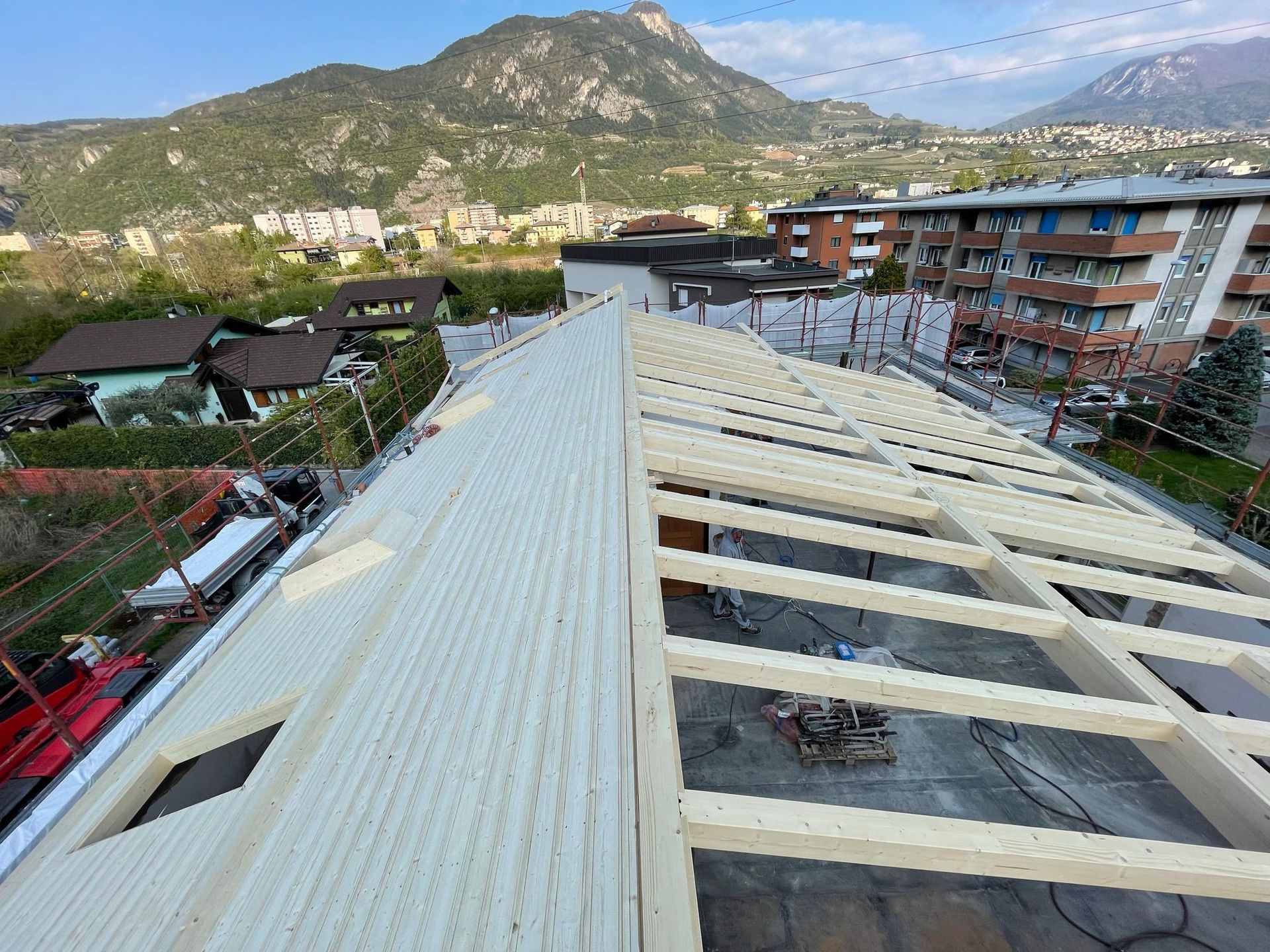 Vista dall'alto del tetto di un edificio in costruzione, che mostra i pannelli bianchi già rifiniti sulla sinistra e le travi in ​​legno a vista.