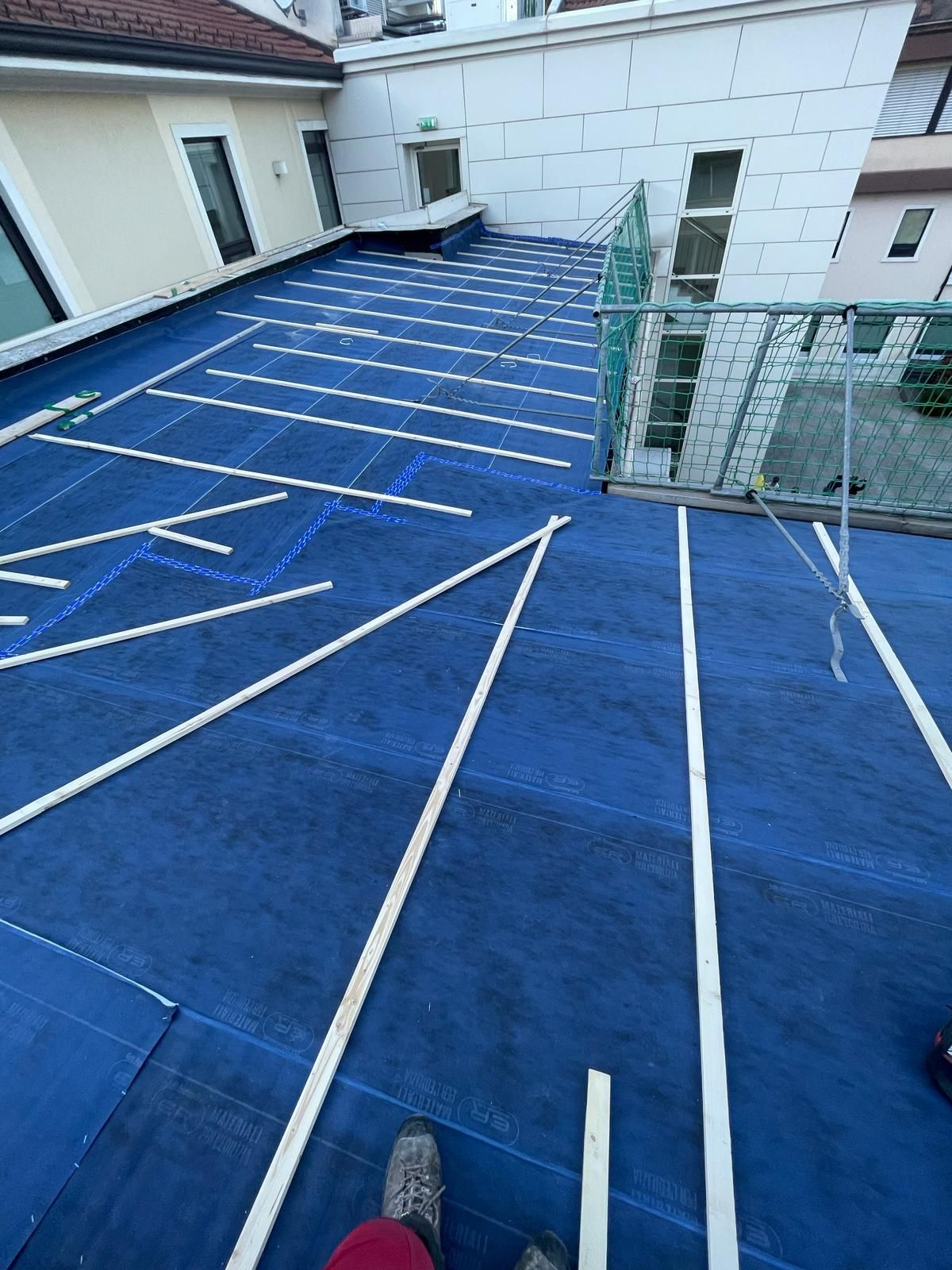 Vista dall'alto di un operaio edile di un tetto piano blu in riparazione, caratterizzato da guide bianche disposte a griglia.