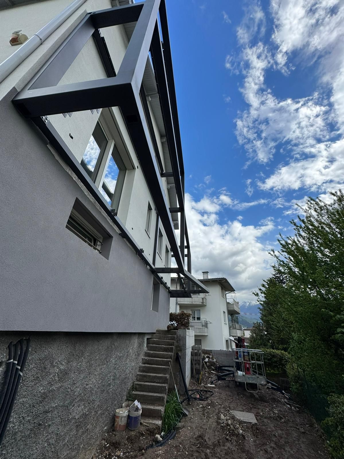 Vista dal basso dell'esterno di un edificio residenziale con una struttura in metallo nero fissata alla parete sopra le scale.