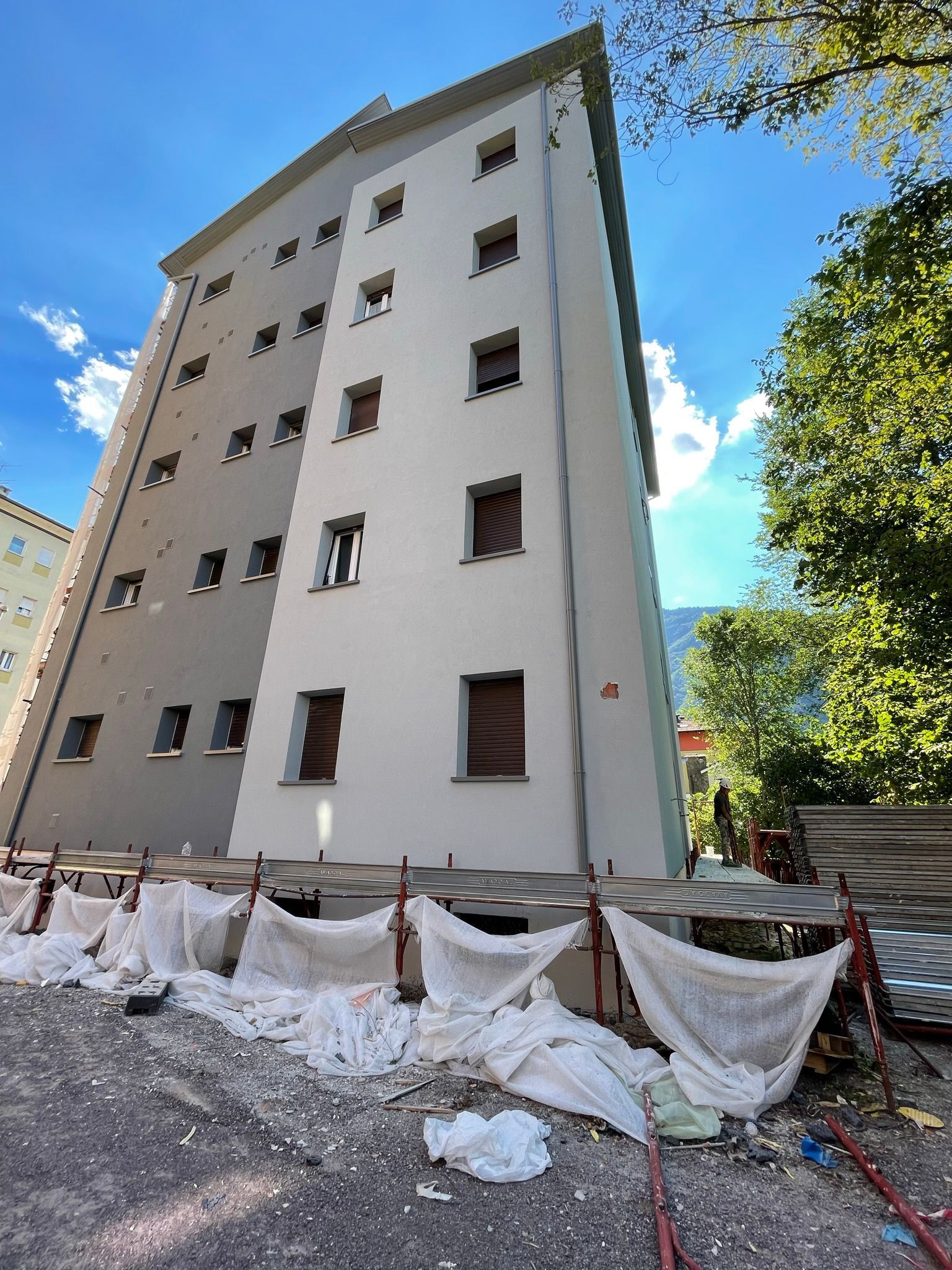 Un edificio residenziale alto e moderno con pannelli grigi e bianchi, visto da un'angolazione bassa, con detriti di costruzione alla base.