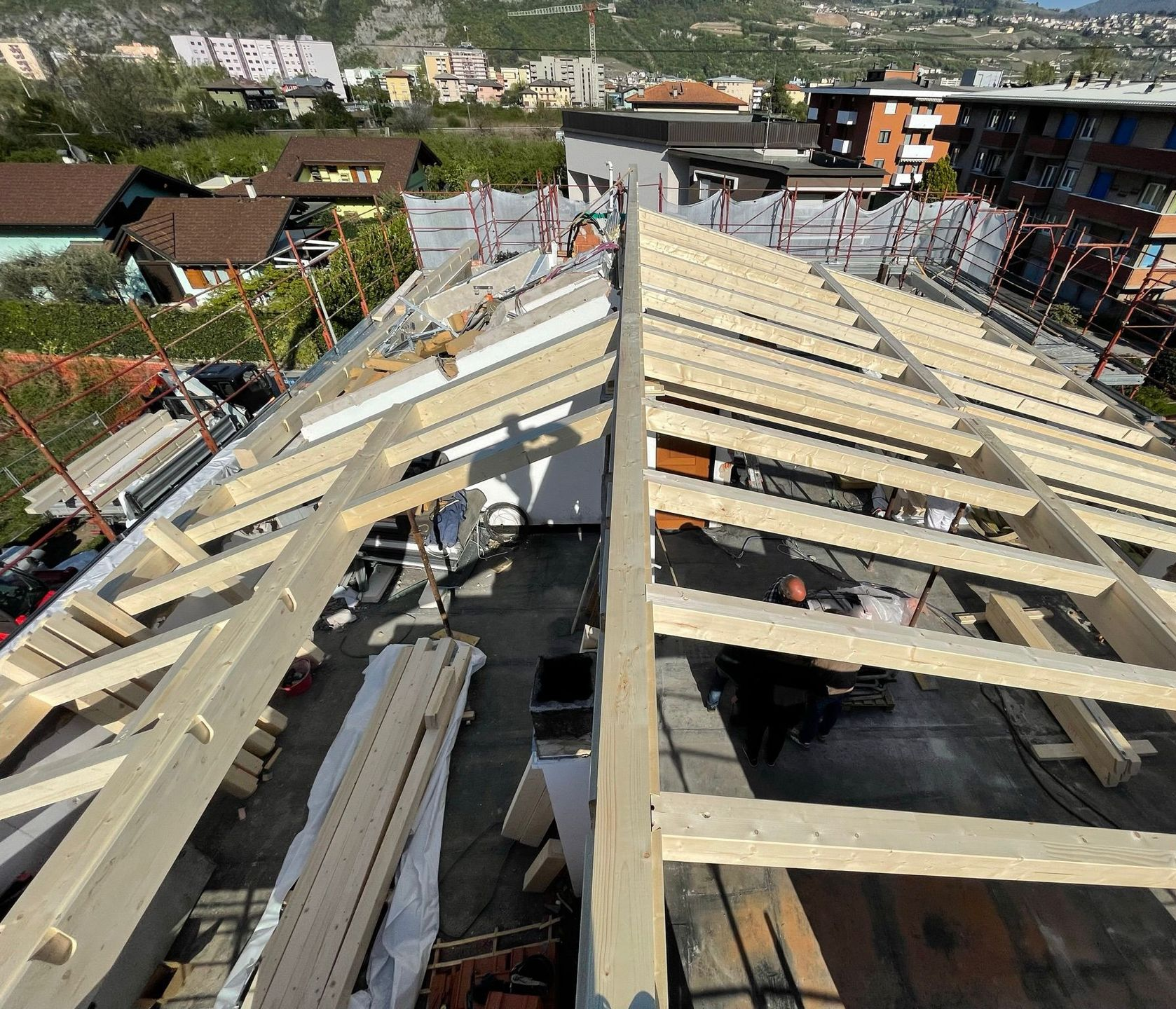 Veduta aerea delle travi di legno in fase di installazione su un edificio in costruzione, con una città visibile in lontananza.
