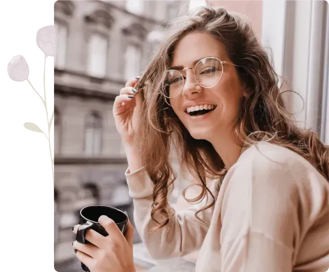 A woman wearing glasses is holding a cup of coffee and smiling.