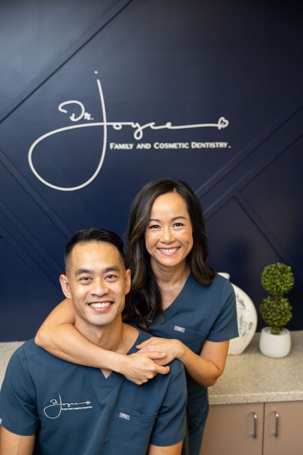 A man and a woman are posing for a picture in front of a sign that says joyce family and cosmetic dentistry.