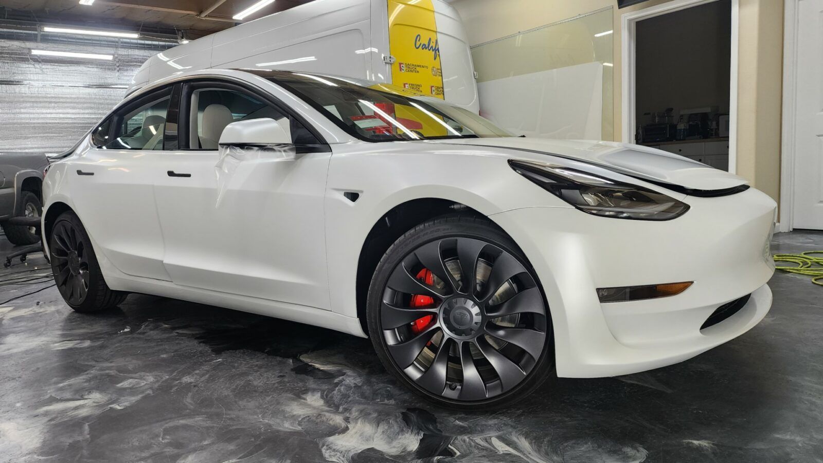 A white tesla model 3 is parked in a garage.