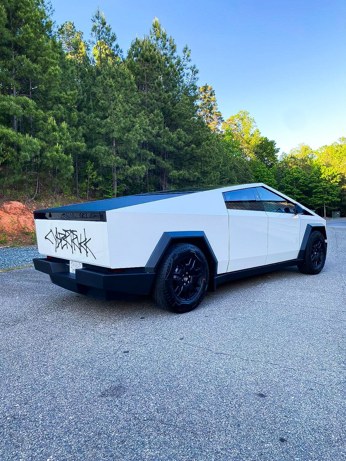 A white tesla cybertruck is parked on a gravel road.