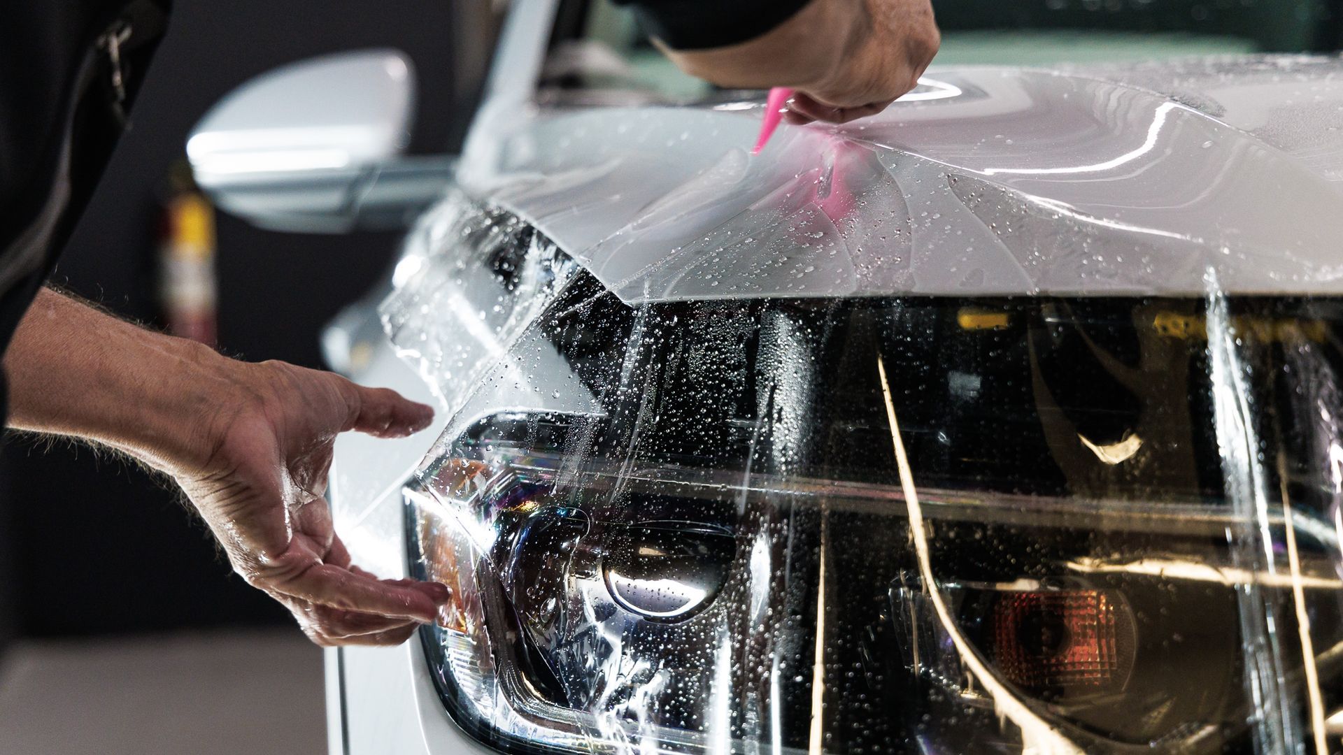 A man is applying a protective film to the hood of a car.