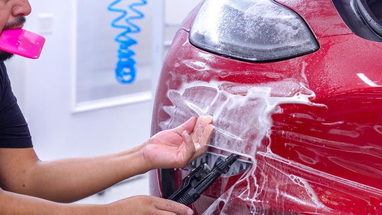 A man is applying a protective film to the front of a red car.
