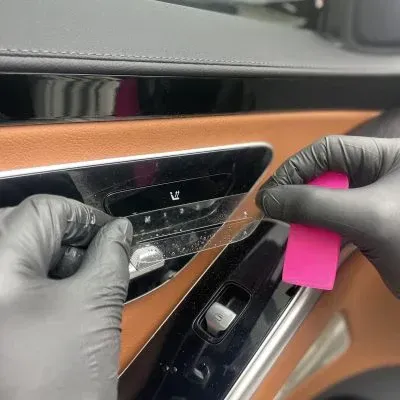 A person wearing black gloves is cleaning the inside of a car door.