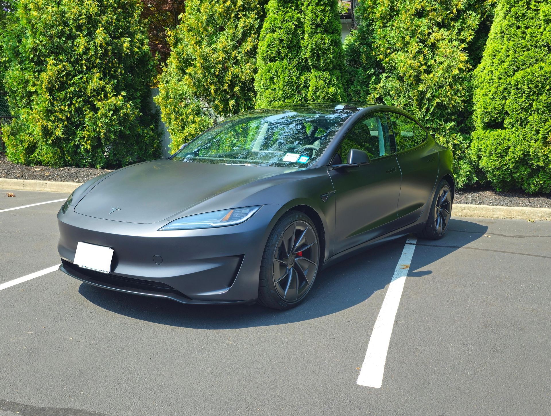 A black tesla model 3 is parked in a parking lot.