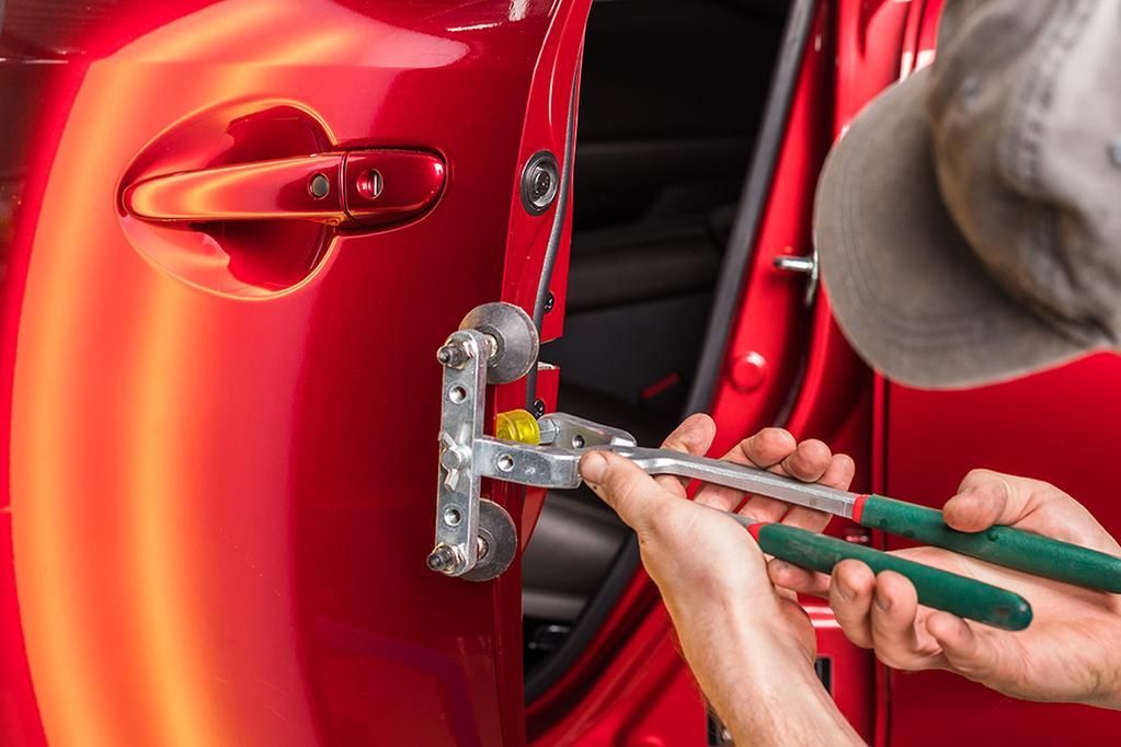 A man is working on a red car door with a pair of pliers.