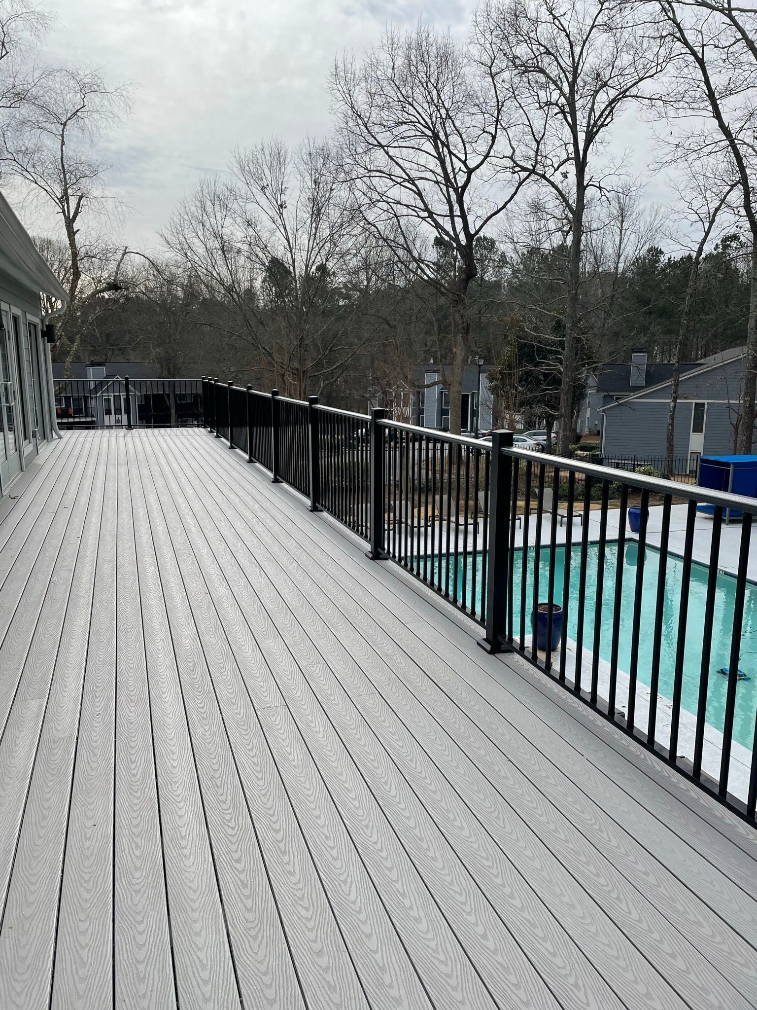 A wooden deck with a metal railing and a pool in the background.