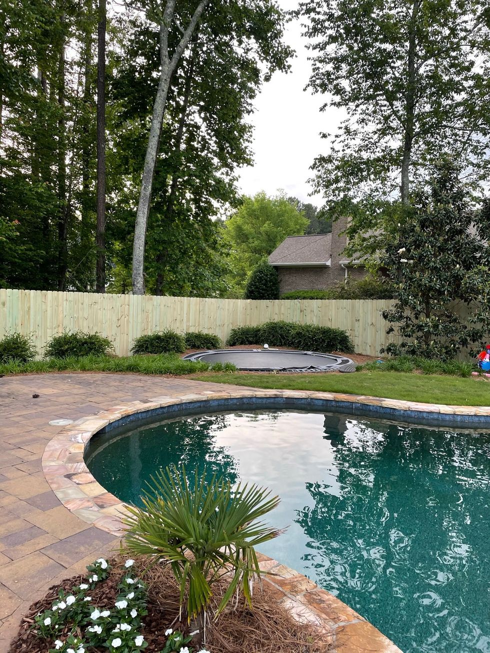 A large swimming pool is surrounded by trees and a privacy fence.