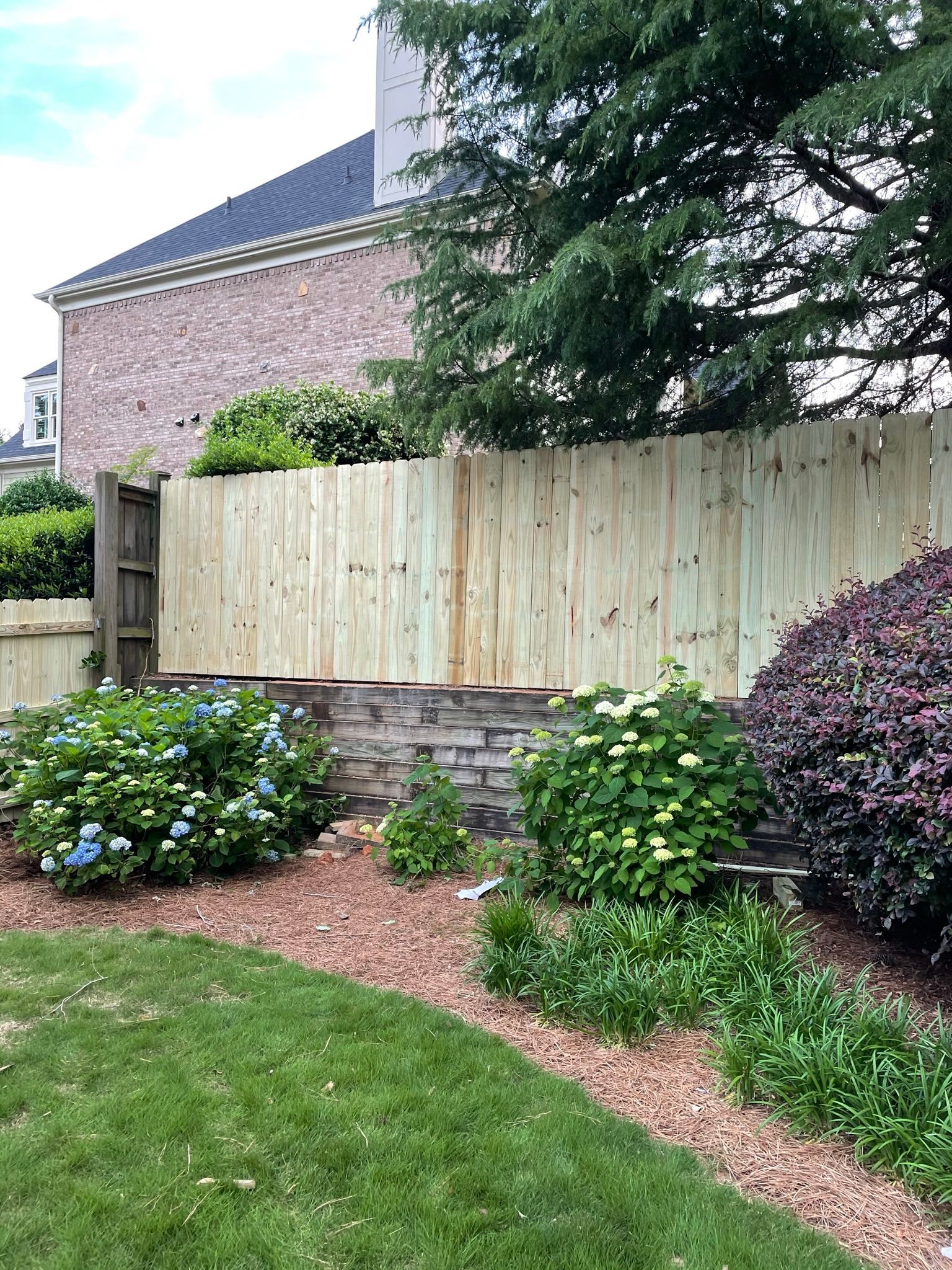 A stockade wooden fence is surrounded by flowers and bushes in a backyard.