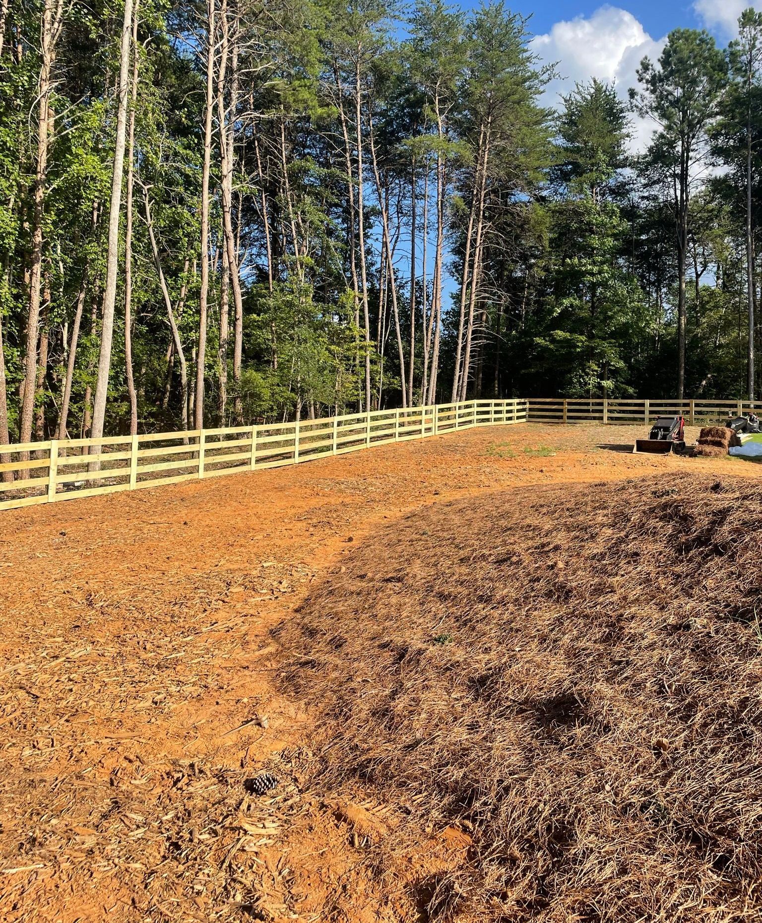 A dirt field with a split rail fence and trees in the background.