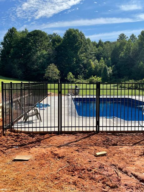 A fence surrounds a swimming pool with trees in the background
