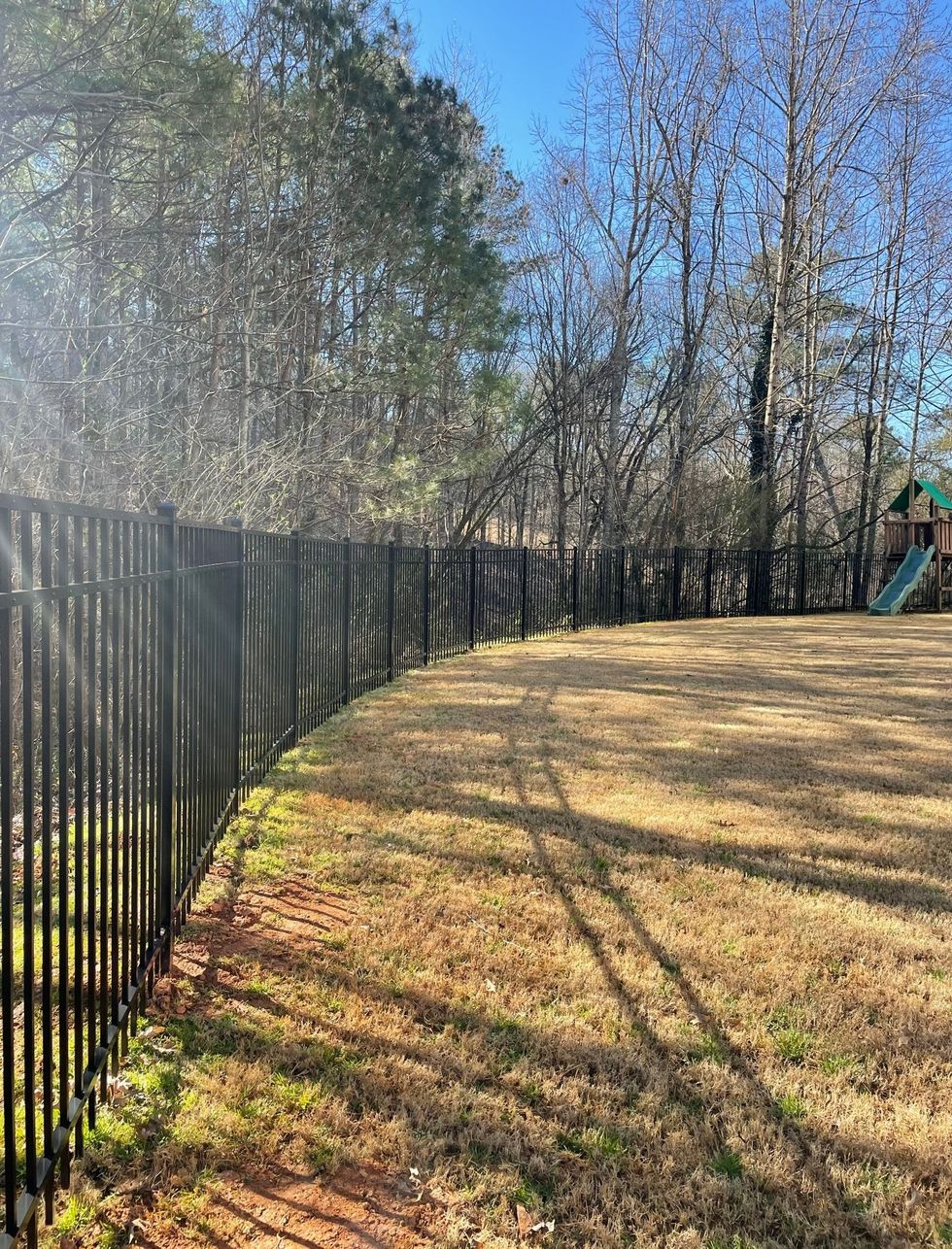 A black fence surrounds a playground in a park.