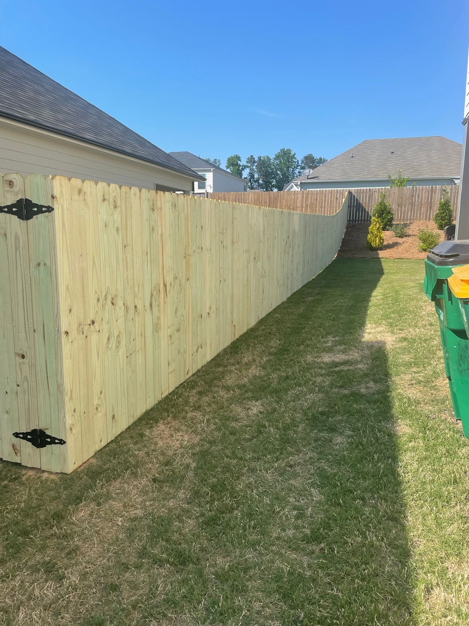 A stockade wooden fence is sitting in the grass in front of a house.