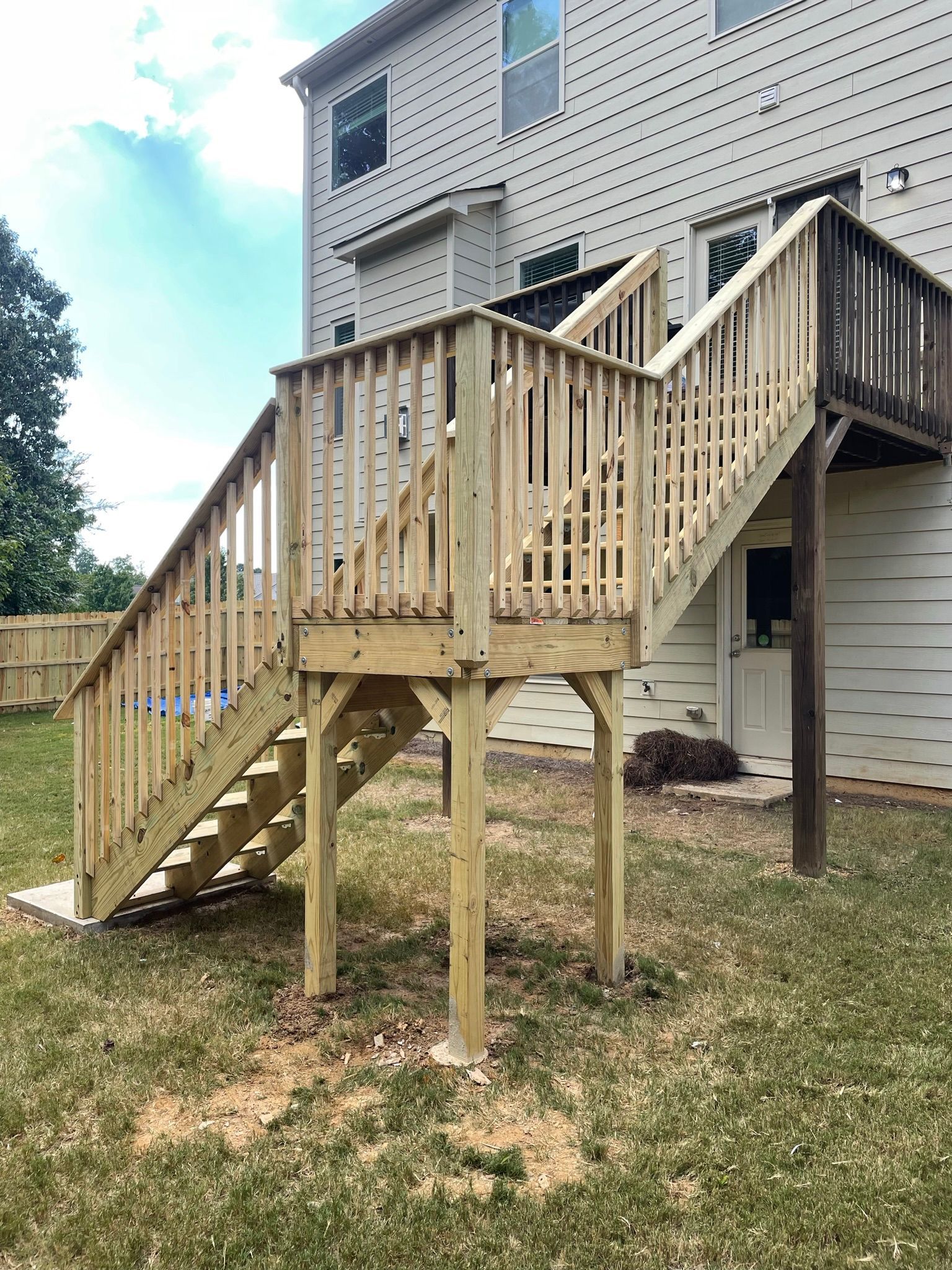 A wooden deck with stairs leading up to it is in the backyard of a house.