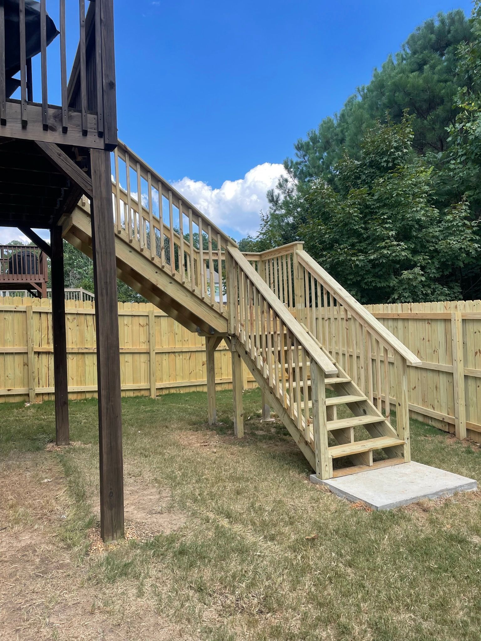 A wooden deck with stairs leading up to it and a fence in the background.