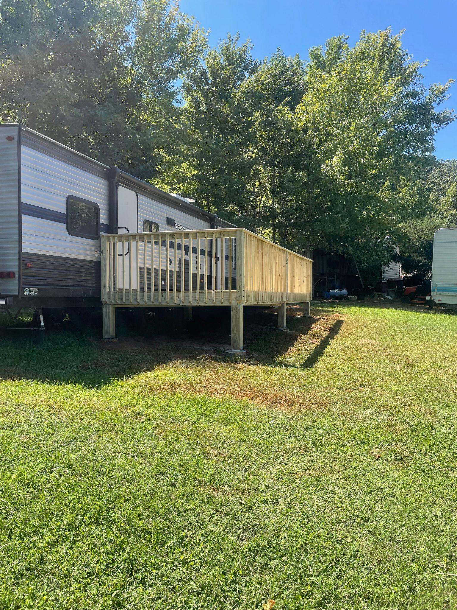 A trailer with a wooden deck is parked in a grassy field.
