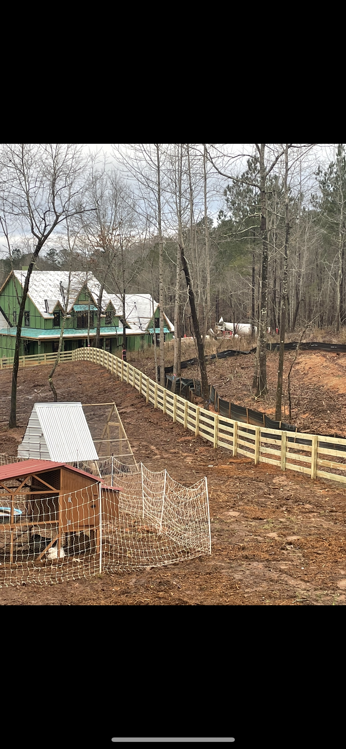 A split rail wooden fence surrounds a farm with a house in the background.