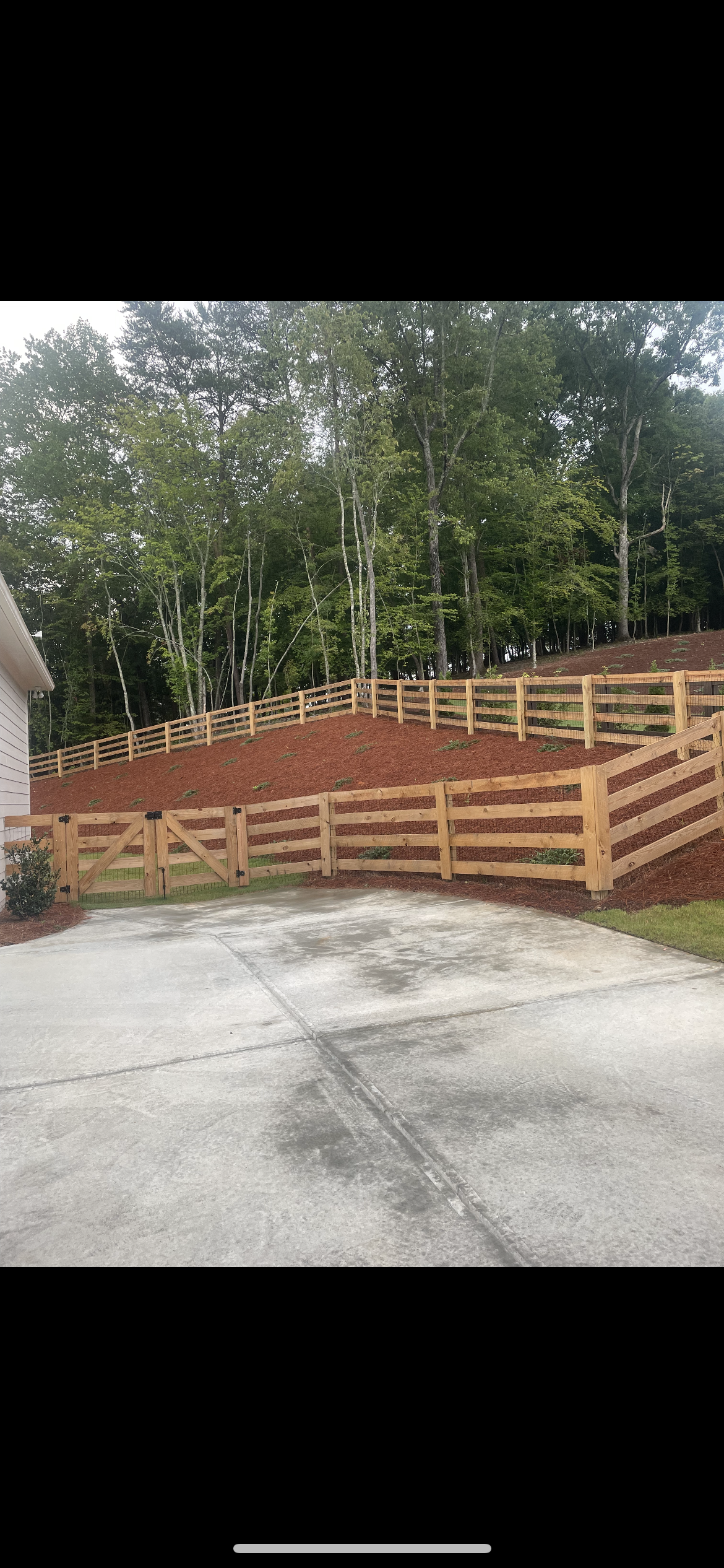 A wooden fence is sitting on top of a dirt hill next to a house.