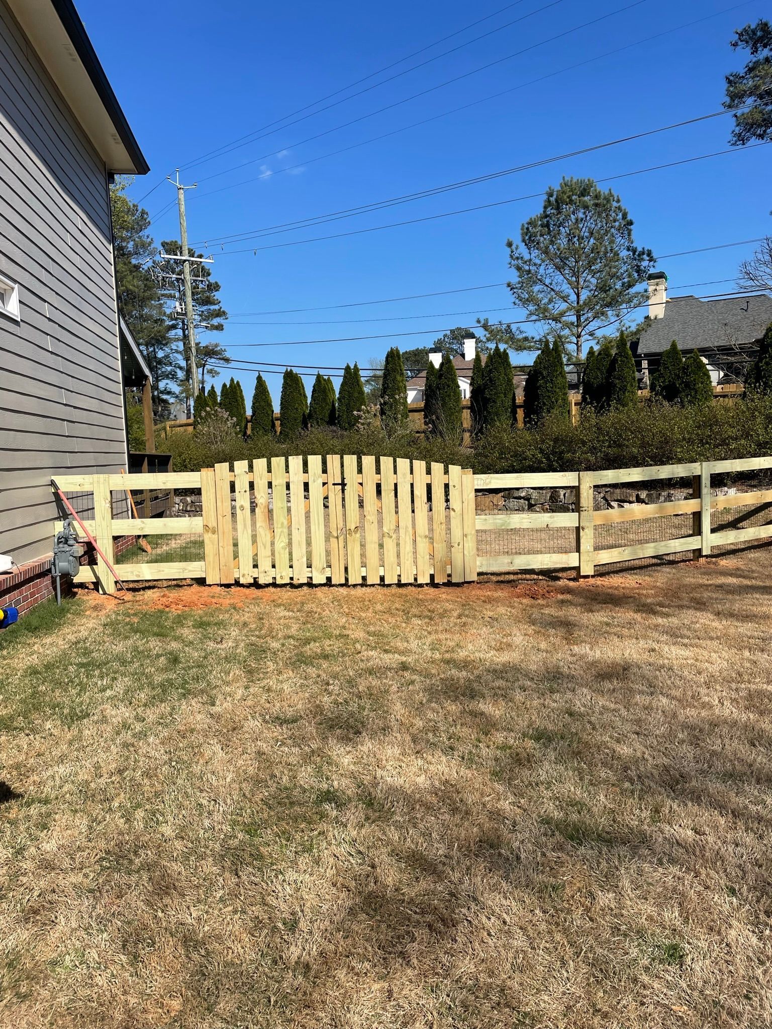 A wooden fence with a gate is in the backyard of a house.