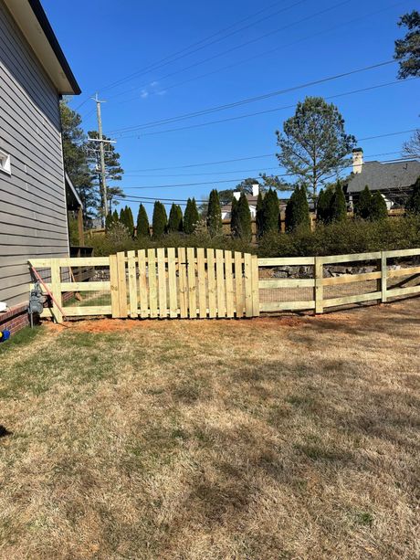 A wooden fence with a gate is in the backyard of a house.