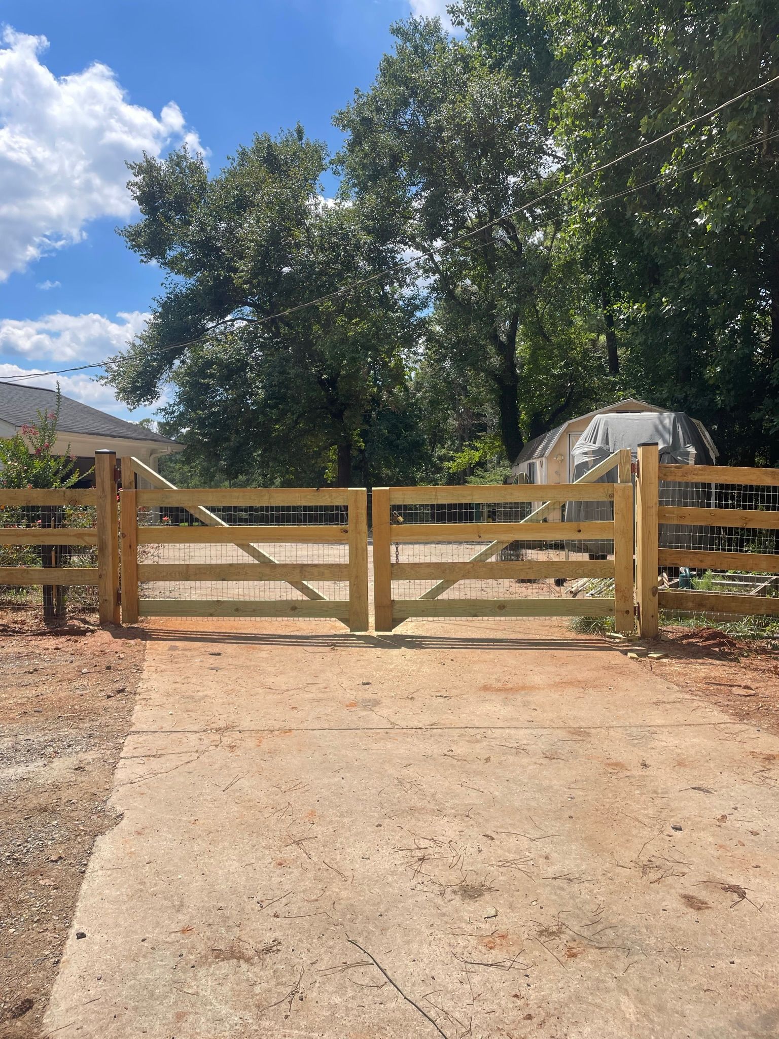 A wooden gate is sitting on the side of a dirt road.