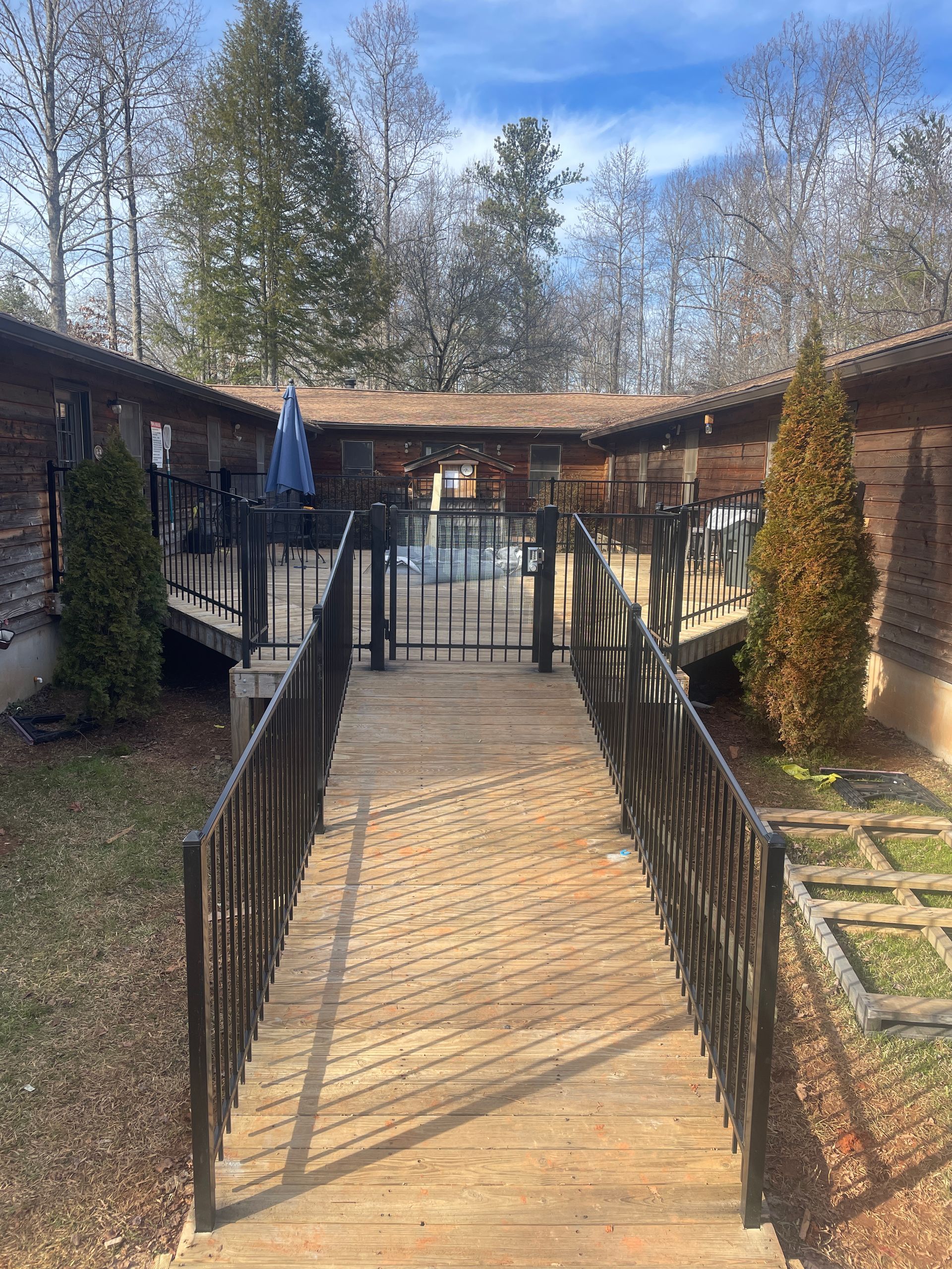 A wooden walkway leading to a house with a fence and metal railing