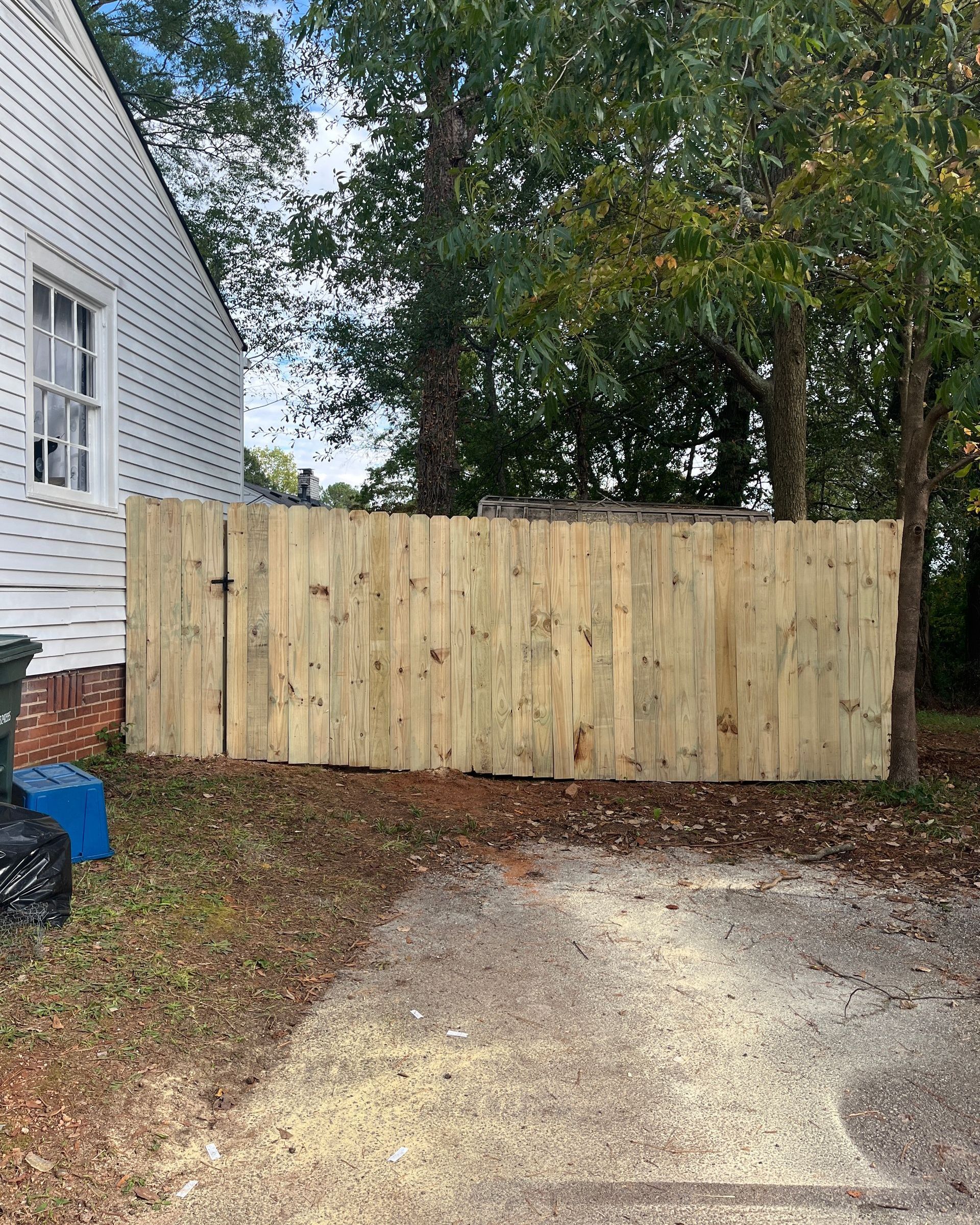 A privacy wooden fence is sitting in front of a white house.
