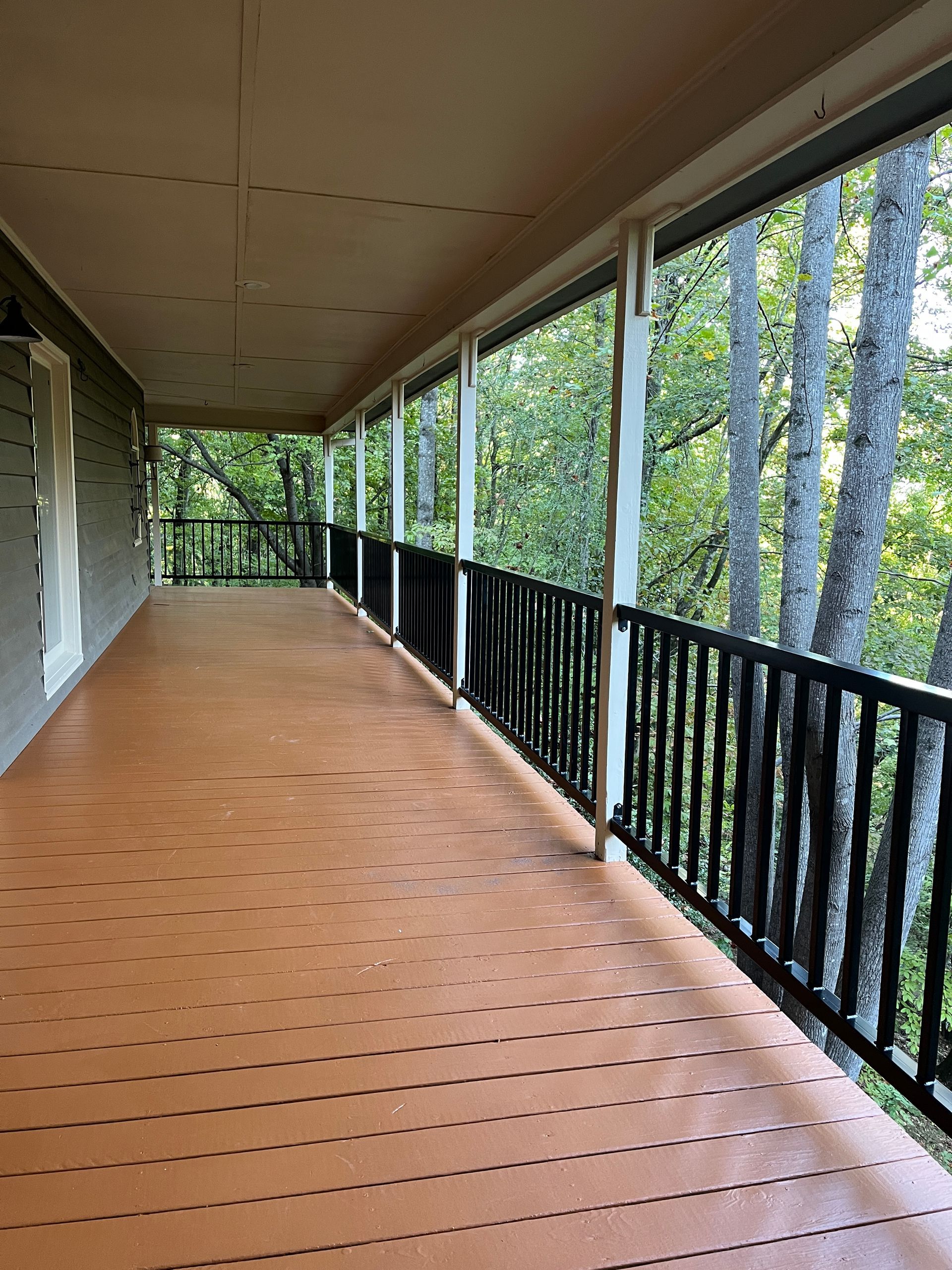 A long wooden porch with a black railing and trees in the background.