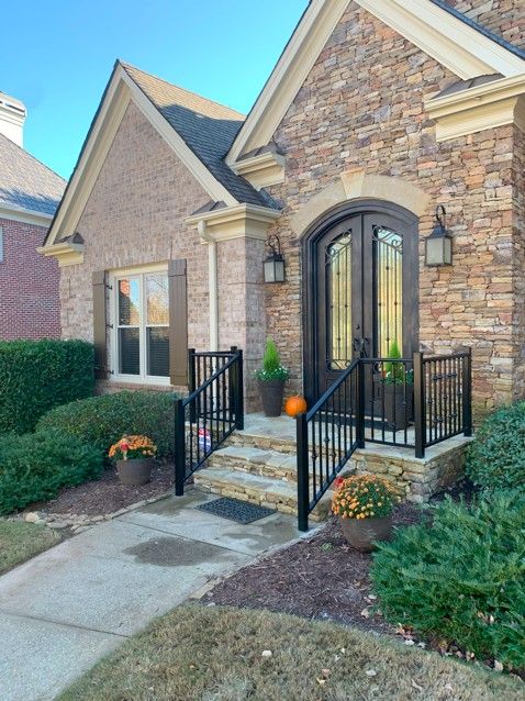 A brick house with a black door and stairs with custom railing
