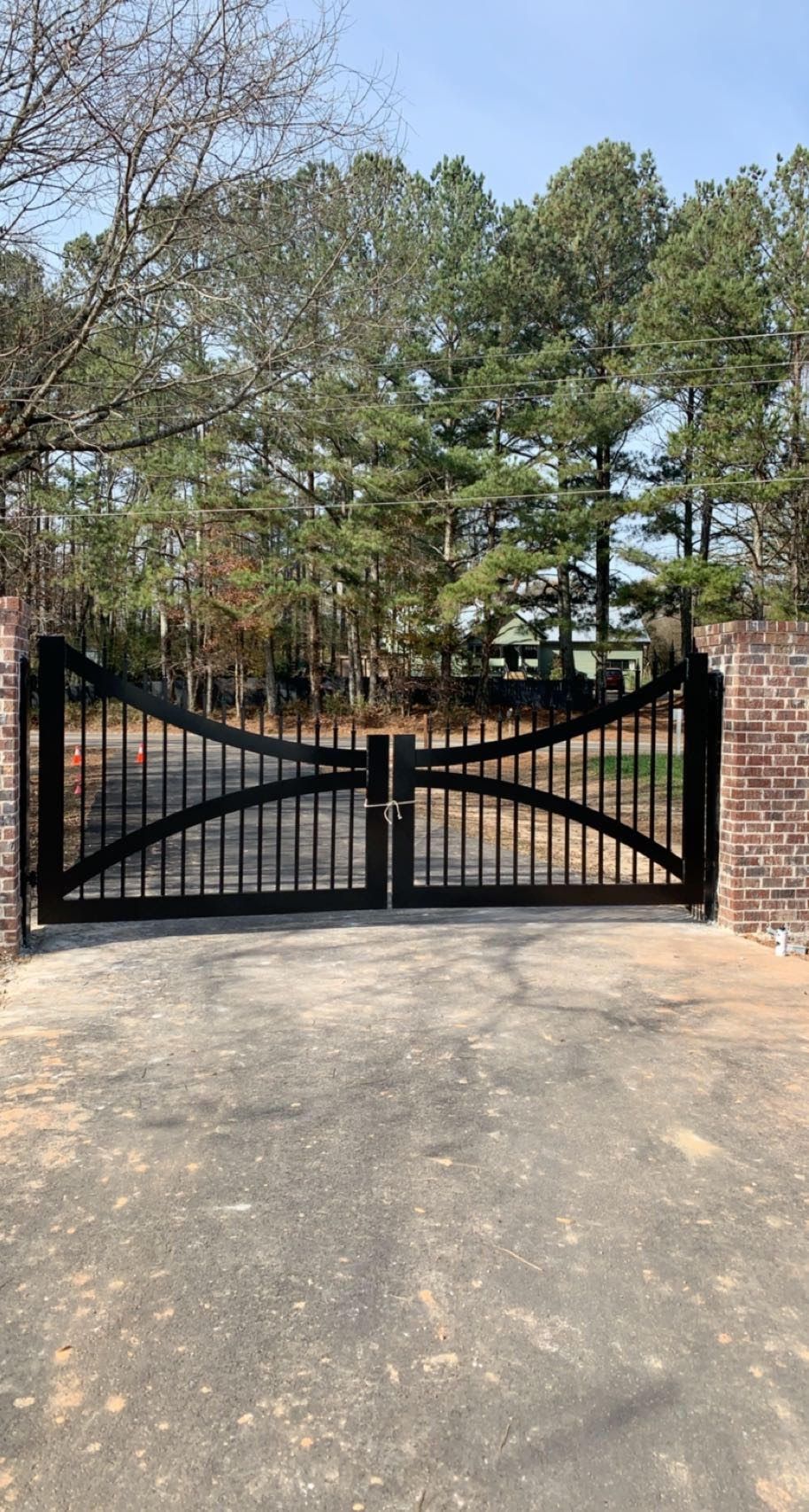 A black entrance gate is sitting in the middle of a driveway next to a brick wall.